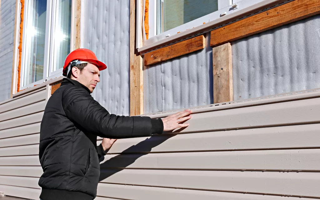 A worker installs panels beige wood siding on the facade of the house