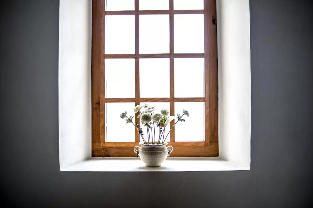 A wood window with a vase of white daisies placed on the sill