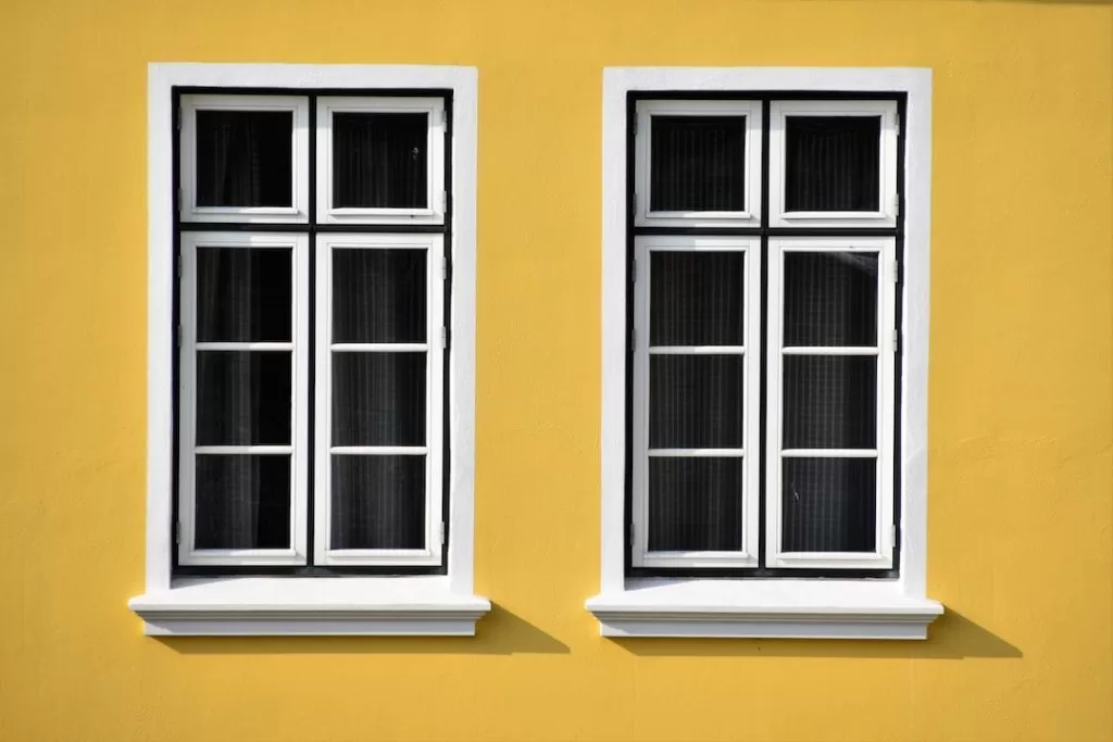 Two windows with a white finish on a bold yellow home exterior
