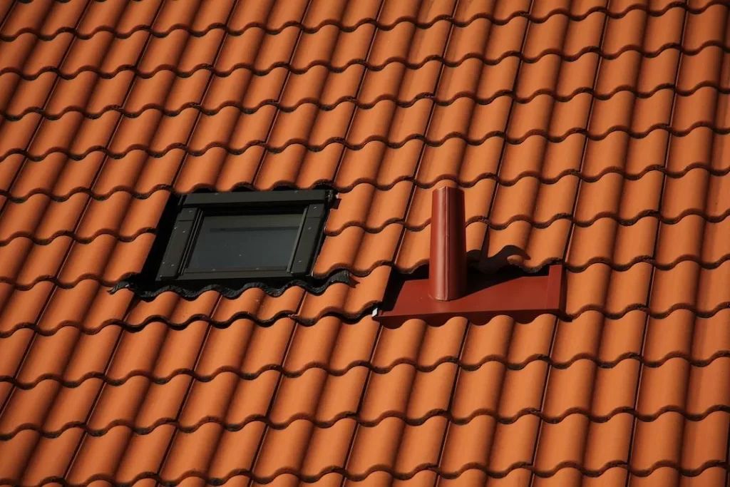 A new, dark tan tile roof on a home with a black, framed window and red vent