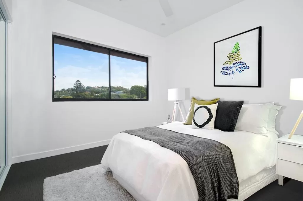 Large vinyl windows with black frames allow natural light into a bedroom with white accents