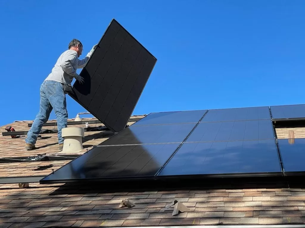 A man installs solar panels on the roof of a residential home