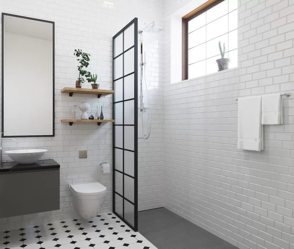 A renovated bathroom with an open-concept shower, white tiles, and plants on shelves.