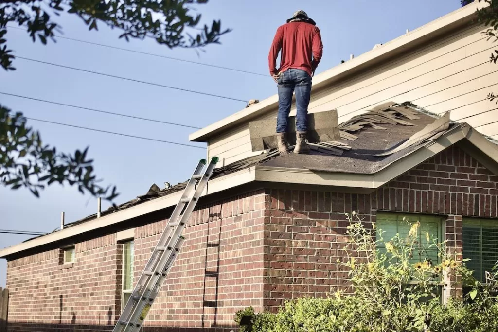 Contractor from local roofing company standing on a roof wearing a red shirt and jeans
