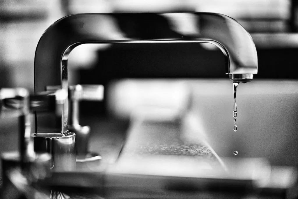 Black-and-white photo of a chrome sink that is dripping water.