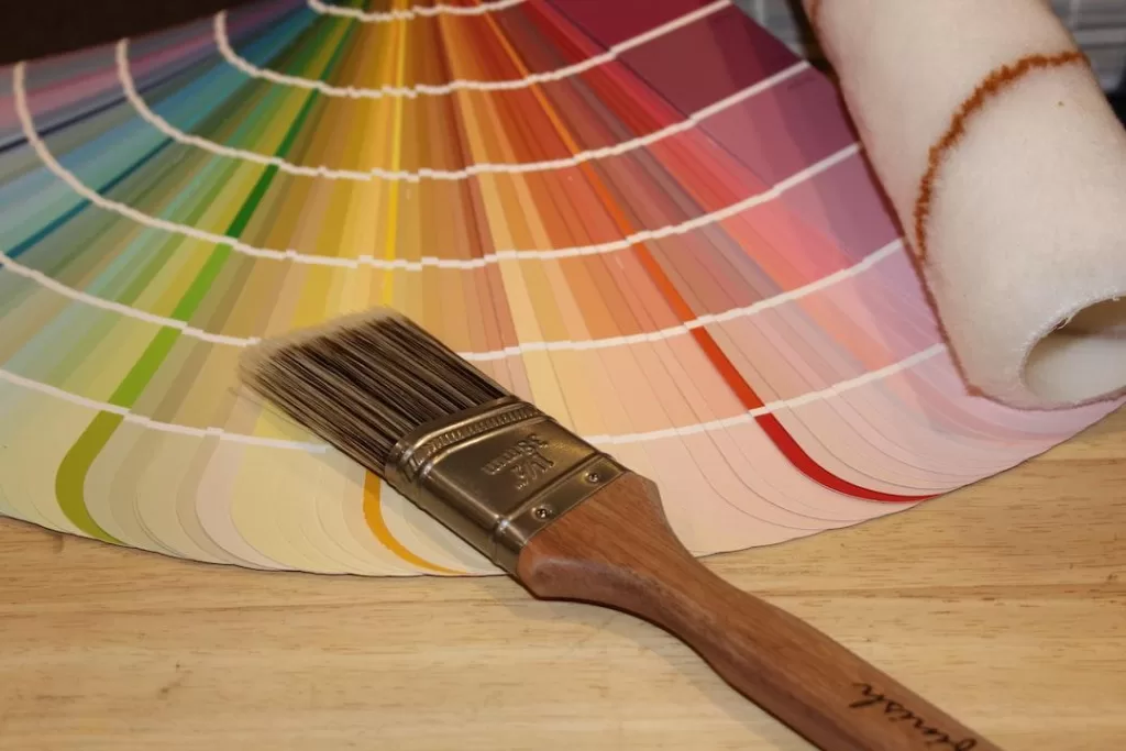 A paint brush laying on top of a variety of paint charts showing different paint colors.