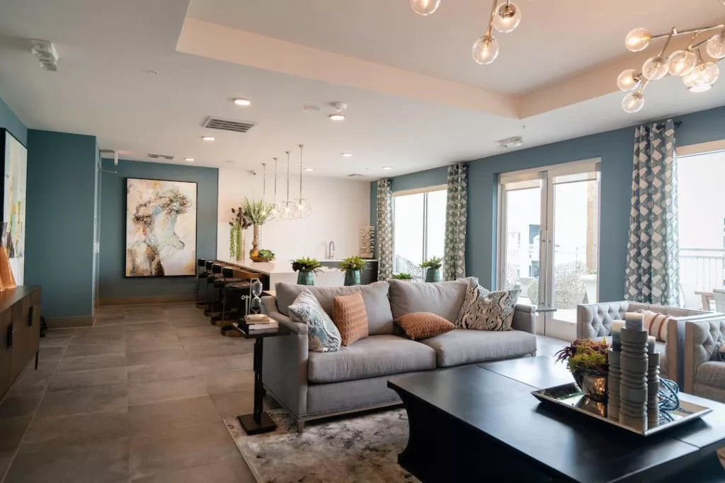 A fully renovated and modern living room with teal walls, a lush grey couch, and pendant lighting