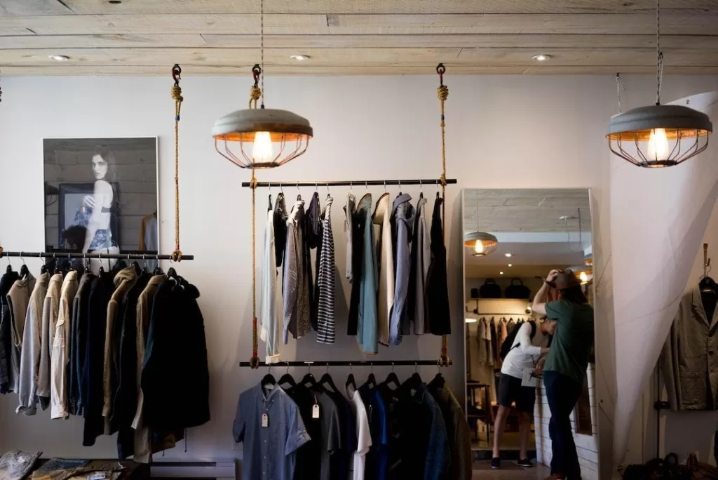 People shop in a clothing store with both pendant lights and recessed lighting.