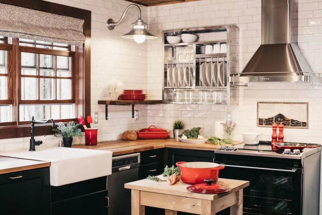 A new kitchen with black cabinetry, chrome appliances, and red kitchenware placed on wooden countertops