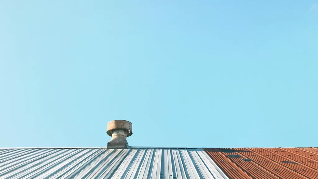 Rustic metal chimney on a corrugated iron roof against a clear blue sky.
