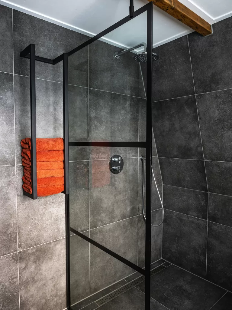 a shower against a backdrop of dark tiles in the bathroom