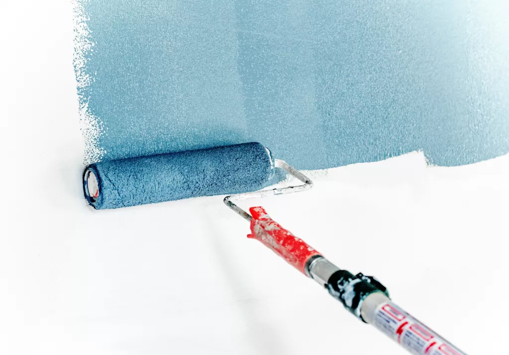 Painting a wall in blue using a roller brush, with a crisp line of freshly applied paint against the white surface.