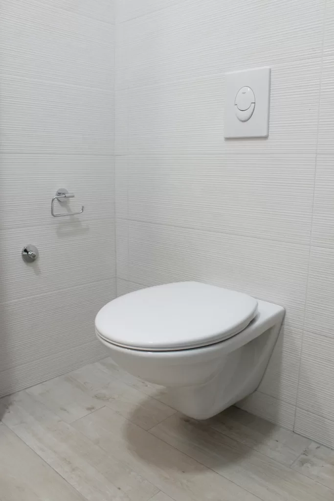 A modern wall-mounted upflush toilet in a minimalist bathroom, featuring white textured walls and light wooden flooring.